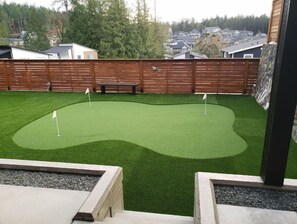 Een achtertuin met kunstgras, een houten omheining en een stenen bank.
