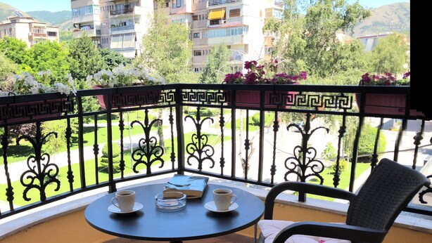 Un balcón con una mesa redonda y dos sillas, vista a una zona residencial y cielo despejado.