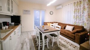 Un espacio habitable ideal para familias, con una mesa de comedor, sillas blancas, un sofá marrón y una zona de cocina con armarios y una máquina de café.