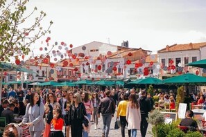 Un mercado al aire libre animado, con gente caminando y cenando bajo sombrillas verdes.