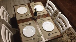 Mesa de comedor dispuesta para cuatro personas, con sillas blancas, una botella de vino y copas de vino.