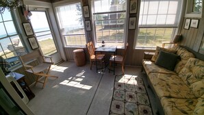 A sunlit room with a view of the sea, a wooden table with chairs, a patterned rug, and a sofa. - Stunning House on the Bay in the Beautiful Upper Penninsula of Michigan (Cedar River)