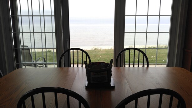 A dining table with four chairs, a bag of potatoes, and a view of the ocean through large windows. - Stunning House on the Bay in the Beautiful Upper Penninsula of Michigan (Cedar River)