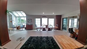 A spacious kitchen with a gas stove, wooden table, and chairs. There is a dining area with a table and chairs, and large windows allowing natural light. - Stunning House on the Bay in the Beautiful Upper Penninsula of Michigan (Cedar River)