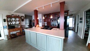 A kitchen with a central island, wooden cabinets, and a dining area with chairs and a table. - Stunning House on the Bay in the Beautiful Upper Penninsula of Michigan (Cedar River)