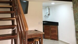 Eine Treppe mit hölzerner Handlauf, die zu einer Landung im zweiten Stock führt. Darunter ist ein Küchenbereich mit schwarzer Arbeitsplatte und Schränken zu sehen.