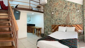 Ein Schlafzimmer mit Bett, Holz-Kopfteil, einer Treppe, einem Schreibtisch und einer Küchenzeile.