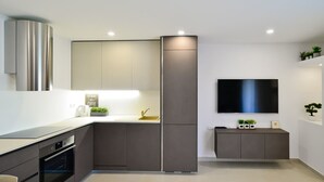 Una cocina moderna con horno empotrado, un lavamanos y un televisor de pantalla plana montado en la pared.
