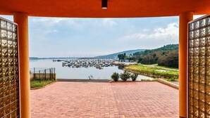 Una terraza cubierta con vistas a un puerto deportivo y un lago, con suelo de ladrillo y paneles de vidrio.