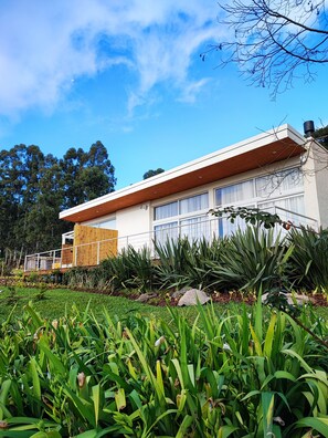 A modern house with a flat roof, large windows, and a wooden deck. - Vila Nambu (Gramado)