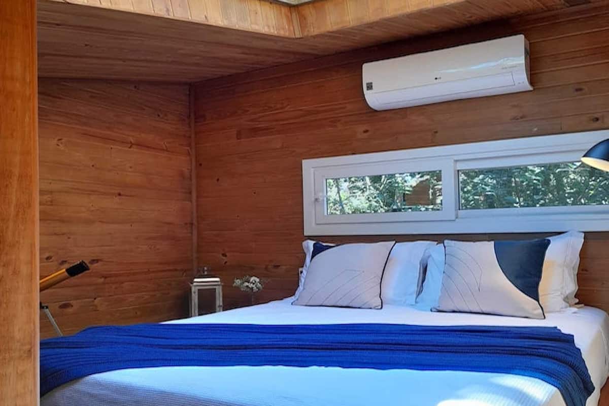 A wooden room with a bed, skylight, and an air conditioning unit.