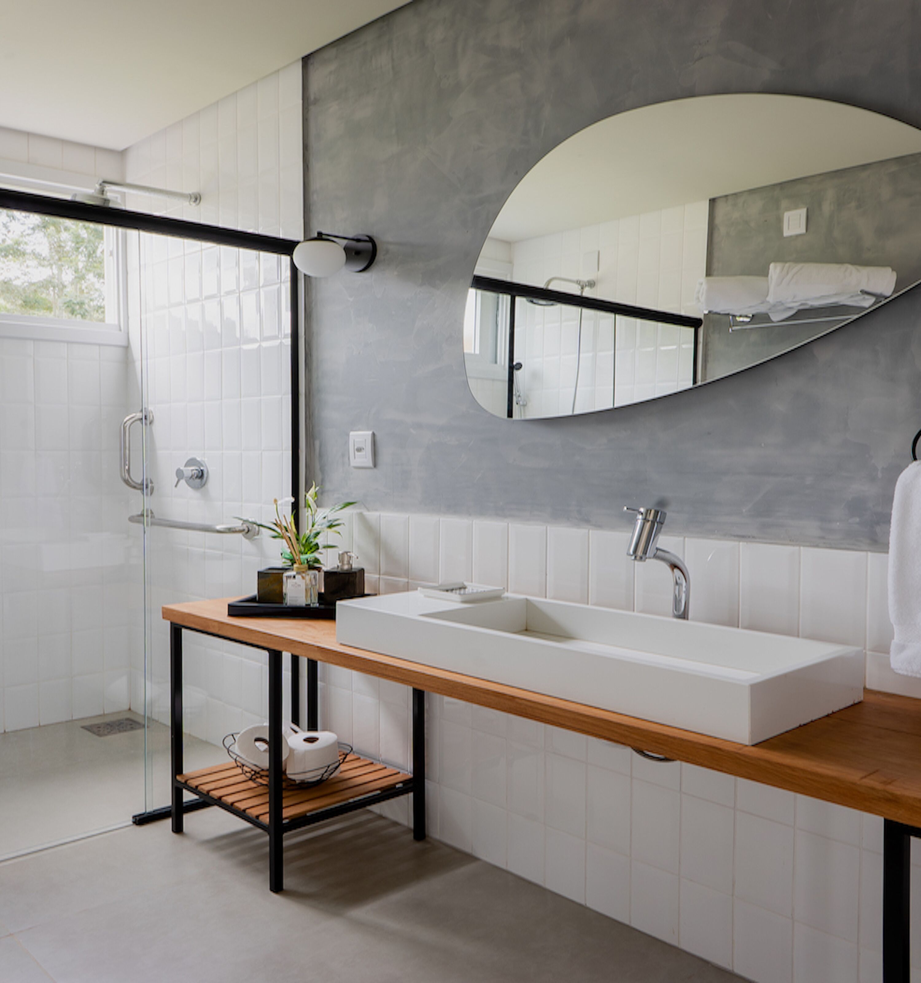 A modern bathroom with a large white sink, a wooden vanity, a glass shower enclosure, and a large mirror.