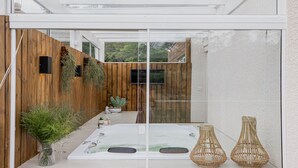 A modern outdoor bathroom with a glass enclosure, wooden fence, and two wicker vases. - Vila Nambu (Gramado)