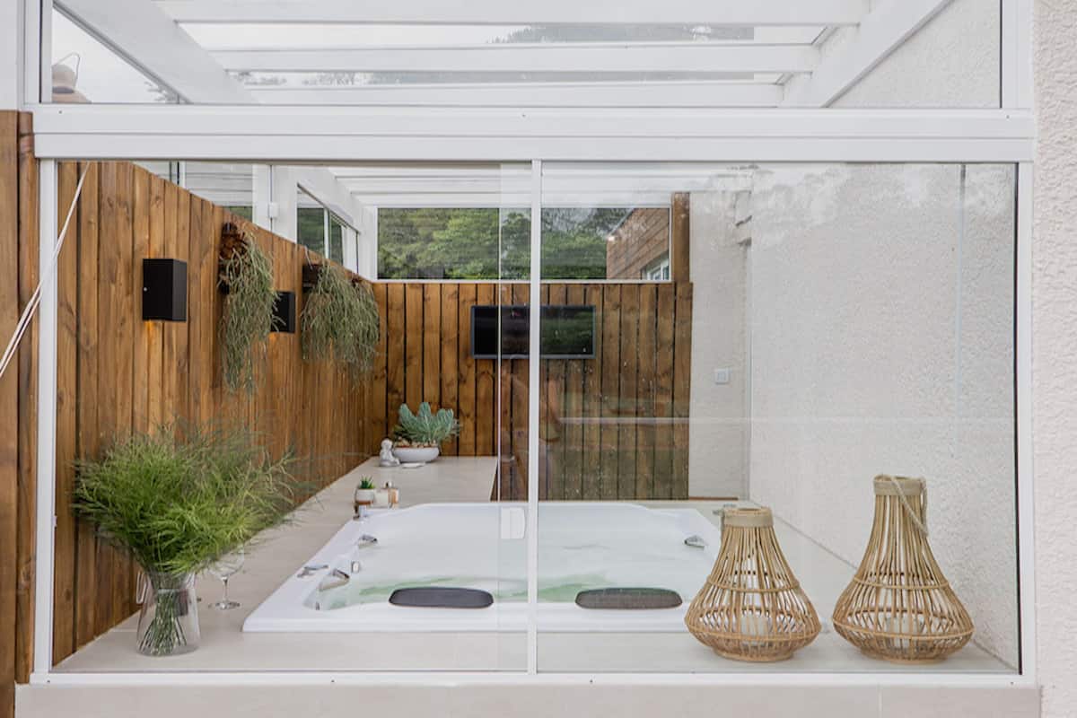 A modern outdoor bathroom with a glass enclosure, wooden fence, and two wicker vases.