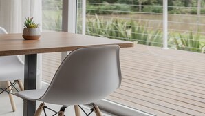 A modern dining area with a wooden table, a white chair, and a potted plant. - Vila Nambu (Gramado)