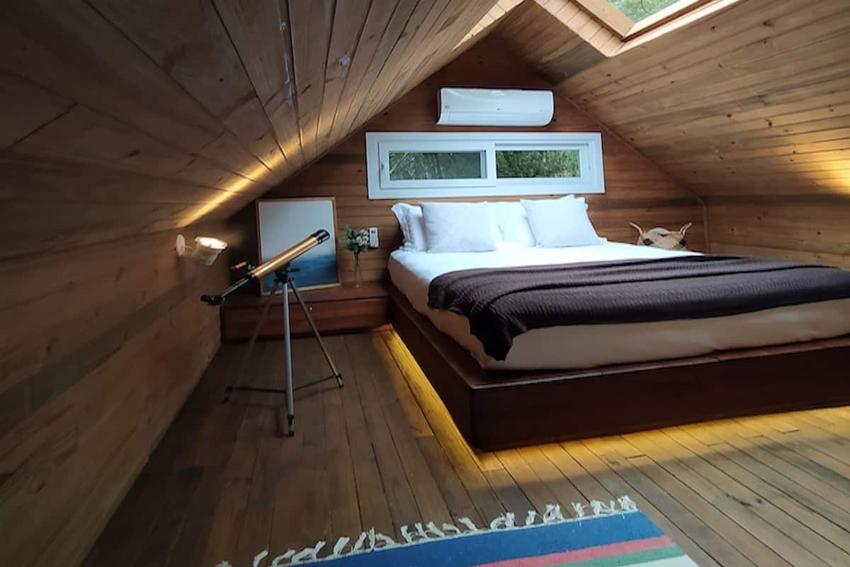 A cozy attic bedroom with a skylight, a telescope, and a colorful rug.