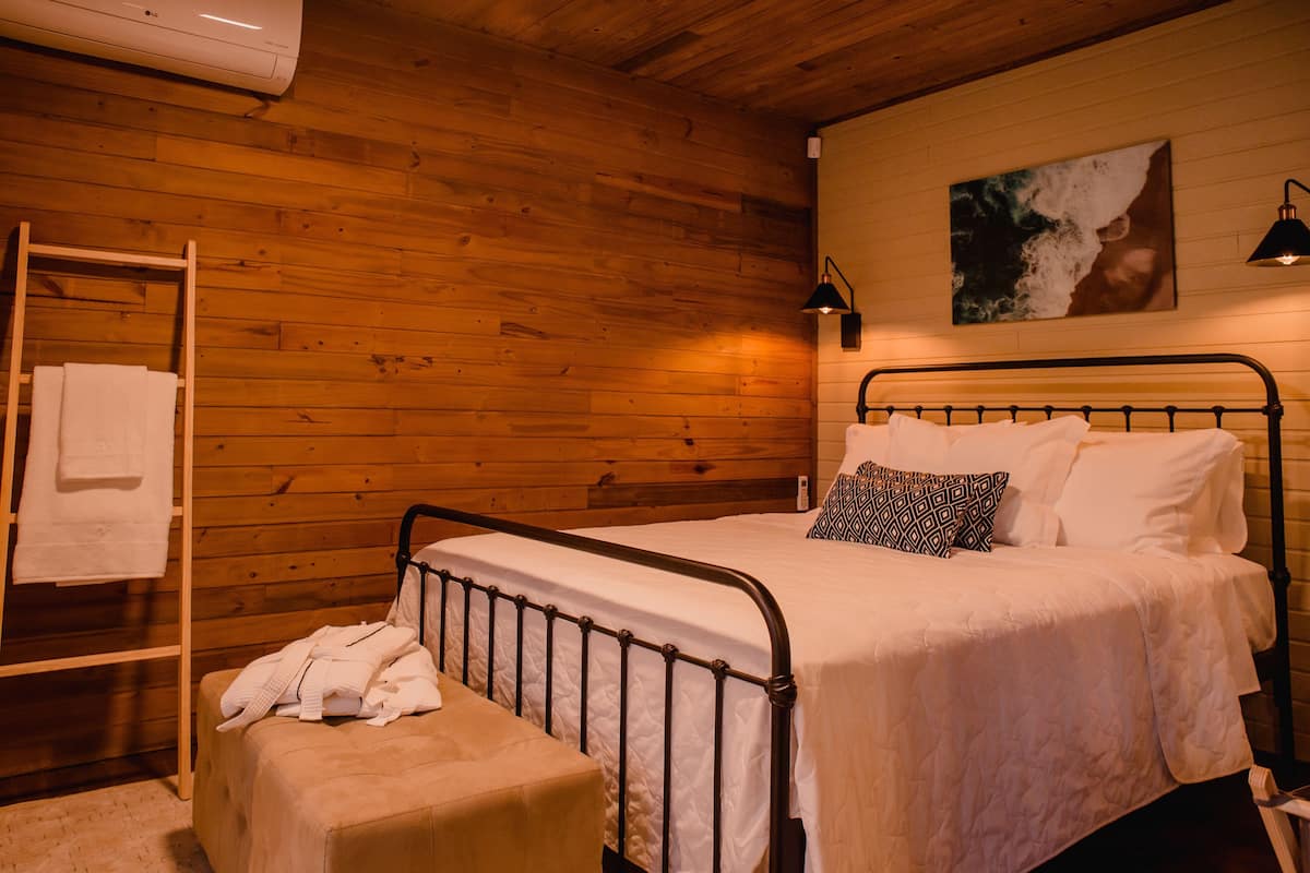 A wooden-paneled room with a bed, a towel rack, and a painting on the wall.