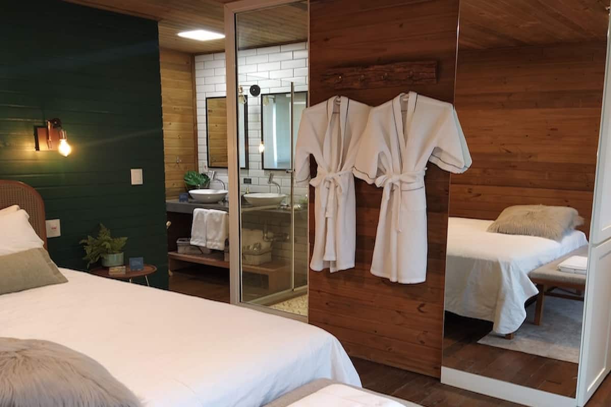 A hotel room with a bed, a bench, a mirror, and a bathroom visible through a sliding door.