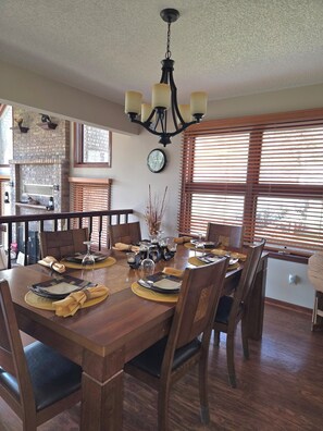 A dining area with a wooden table set for four, a chandelier, and a brick fireplace. - Lake front, pool and golf access, Sand Valley, Lake Arrowhead- 3 king beds! (Nekoosa)