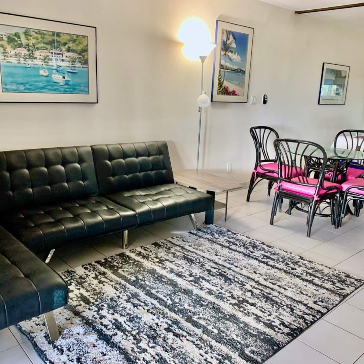 Un salon avec un canapé en cuir noir, un tapis à motifs et un coin repas comprenant des chaises et une table en métal.