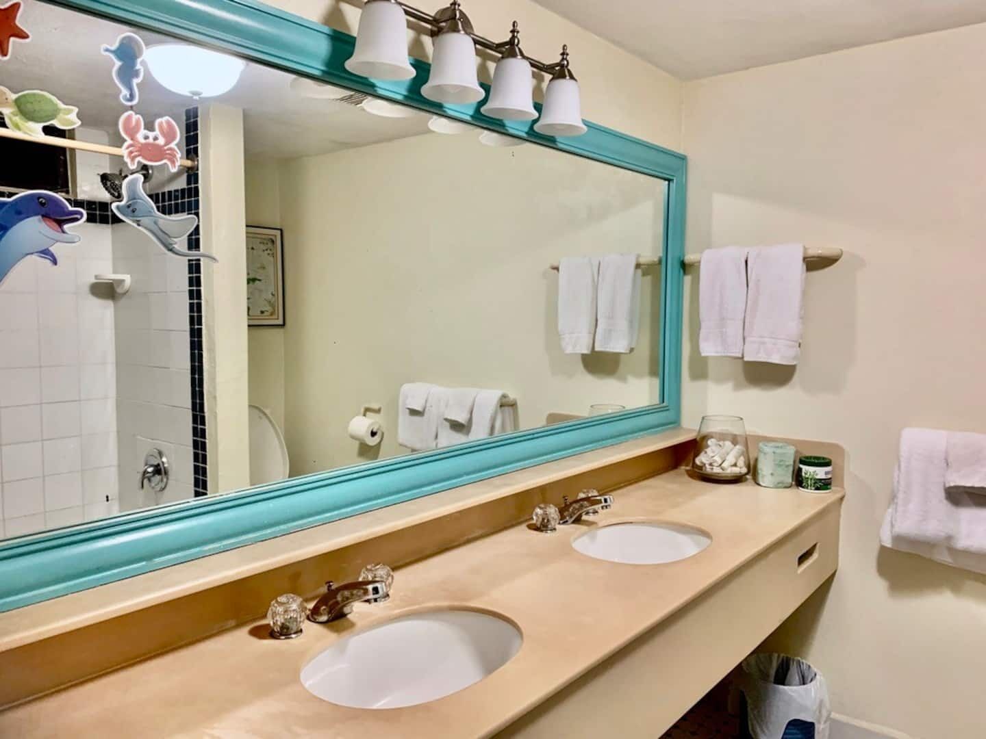 Un baño con dos lavamanos, un espejo grande y un perchero para toallas.