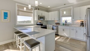Una cocina moderna con armarios blancos, una isla central con taburetes de bar, electrodomésticos de acero inoxidable e iluminación colgante.