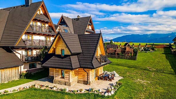 Une cabane en rondins dotée d’un balcon, entourée d’une pelouse bien entretenue et avec une chaîne de montagnes en toile de fond.