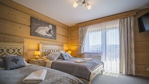 Une pièce en bois avec deux lits, un lustre, un tableau et une fenêtre avec des rideaux.