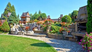 Un jardin avec des allées pavées de pierres, des bâtiments rustiques et une végétation luxuriante.