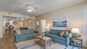 A living room with two sofas, a coffee table, and a lamp. There is a painting on the wall and a ceiling fan. - $150 activities - E-gift card when you book - Balcony Access from Every Bedroom | Oceanview | MG1108 (Myrtle Beach)