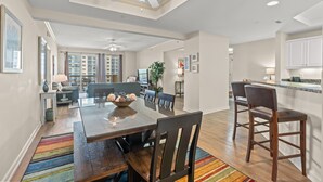 A spacious dining area with a wooden table and chairs, a ceiling fan, and a view of the living room and kitchen in the background. - $150 activities - E-gift card when you book - Balcony Access from Every Bedroom | Oceanview | MG1108 (Myrtle Beach)