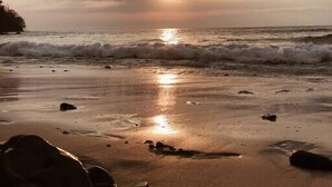 A beach with the sun setting over the horizon, waves gently crashing onto the shore, and a few scattered rocks. - Jungle Treehouse w/ Daily Breakfast, WiFi + Views (Cobano)