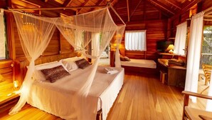 A wooden cabin with a bed under a mosquito net, a desk, and a chair. - Jungle Treehouse w/ Daily Breakfast, WiFi + Views (Cobano)