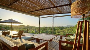 An outdoor deck with wooden furniture, a large umbrella, and a view of a lush landscape. - Casa Blanca | Free Breakfast + Housekeeping | Pool (Cobano)