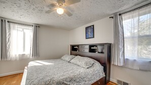 Un dormitorio con cama, ventilador de techo, ventana con cortinas, radiador y estante montado en la pared.