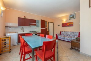Une cuisine compacte dotée d’appareils électroménagers modernes, un coin repas avec des chaises rouges et un canapé recouvert d’un tissu à motifs.