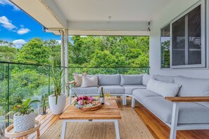 A balcony with a grey sofa, a wooden coffee table with a floral arrangement, and potted plants.