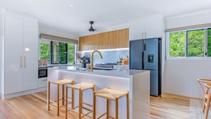 Una cocina moderna con armarios blancos, una isla central con taburetes, horno empotrado y refrigerador.
