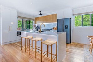 A modern kitchen with a central island, bar stools, and a refrigerator. - Airlie Abode (Jubilee Pocket)