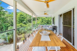 Eine Holzterrasse mit Esstisch und Stühlen, einem Deckenventilator und Blick auf üppiges Grün.