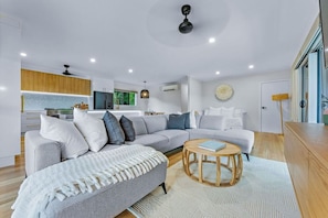 Ein modernes Wohnzimmer mit einem grauen Ecksofa, einem runden Couchtisch aus Holz und einem weißen Hocker.