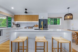 A modern kitchen with a large island, wooden bar stools, and a view of greenery outside. - Airlie Abode (Jubilee Pocket)