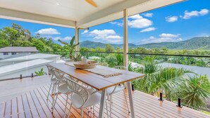 Une terrasse en bois avec une table et des chaises, offrant une vue sur un paysage montagneux.