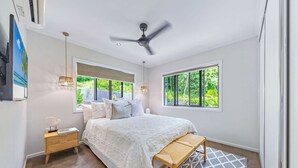 Une chambre à coucher avec un lit, une table de chevet, une lampe et une vue sur la verdure à l’extérieur.