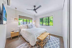 A bedroom with a bed, bedside table, lamp, and a view of greenery outside. - Airlie Abode (Jubilee Pocket)