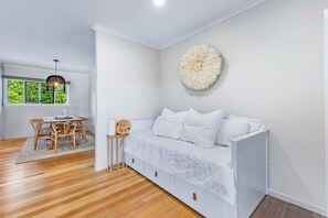 A room with a white sofa, a round wall decoration, a small table with a sign, and a window with a view of greenery. - Airlie Abode (Jubilee Pocket)