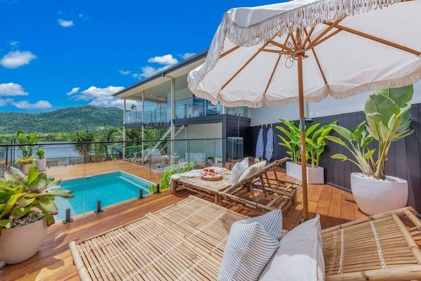 Ein moderner Außenbereich zum Entspannen mit Pool, Liegestühlen und einem großen Sonnenschirm.