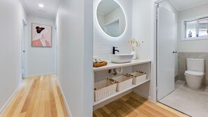 Une salle de bain moderne avec un lavabo blanc, un miroir rond doté d’un éclairage intégré et des toilettes.