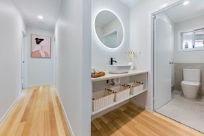 A modern bathroom with a white sink, a round mirror with lighting, and a toilet. - Airlie Abode (Jubilee Pocket)