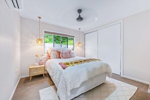Ein Schlafzimmer mit einem Bett, Nachttischen, einem Fenster und einem Deckenventilator.